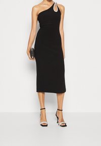 Černé asymetrické šaty s přiléhavým střihem a dekorativním kovovým kroužkem. Doplněné černými páskovými podpatky s akcenty z kamínků.