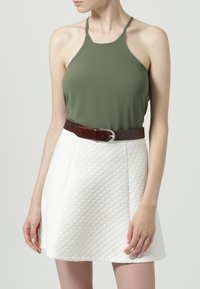 Top halter en verde oliva combinado con una mini falda blanca acolchada, acentuado por un cinturón de cuero marrón con hebilla.
