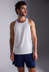 Vitt sportlinne med rund halsringning, tillverkat av ett lätt material, kombinerat med mörkblå shorts, figursydda med en liten logotyp.