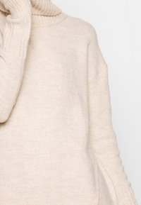 Beige oversize Pullover mit einem hohen, gerippten Rollkragen und gerippten Bündchen, der über eine weiche Textur und überschnittene Schulternähte verfügt.