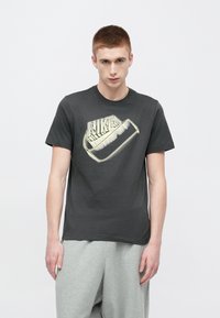 Čierne bavlnené tričko s výrazným logom Nike v svetlej farbe, okrúhlym výstrihom a krátkymi rukávmi, v kombinácii so sivými teplákmi.