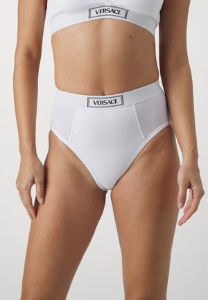 Baltas ribots kokvilnas augstos vidukļa biksītes ar platu elastīgu jostu, uz kuras ir melna "VERSACE" etiķete. Gluda tekstūra un pieguļošs dizains.