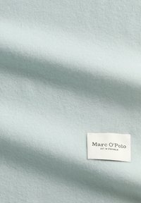 Lichtblauw, zacht textuurstof met een gladde afwerking. Voorzien van een wit label met de tekst "Marc O’Polo EST. IN STOCKHOLM."