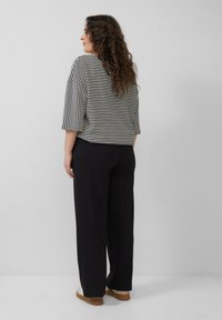 Zwart-wit gestreepte cropped top met wijde mouwen, gecombineerd met losse zwarte broek. Zachte stof met een ontspannen pasvorm, ontworpen voor comfort.