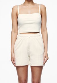 Top corto de color beige claro con tirantes finos, combinado con pantalones cortos con cordón a juego. Hecho de una tela suave y texturizada con un corte relajado.