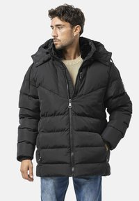 Steppjacke in Schwarz mit Reißverschluss vorne, abnehmbarer Kapuze und gerippten Bündchen; verfügt über horizontale Steppnähte und zwei Vordertaschen.