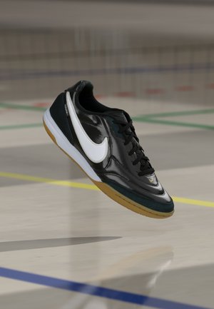 Chaussure de sport noire avec tige en cuir brillant, virgule Nike blanche et semelle extérieure en caoutchouc naturel ; dotée de lacets noirs et de textures contrastées.