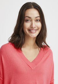 Maglione a maglia corallo con scollo a V, maniche a goccia e polsini a coste. Tessuto morbido con vestibilità rilassata, adatto per un abbigliamento casual.