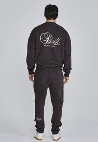 Felpa grigio scuro e pantaloni jogger abbinati in tessuto morbido. Presenta un grande logo bianco sulla schiena e un logo più piccolo sui pantaloni jogger.