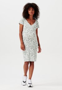 Vestido verde con estampado floral, de escote en V y mangas cortas, que presenta una silueta ajustada y un dobladillo a la altura de la rodilla. Combinado con zapatillas blancas.