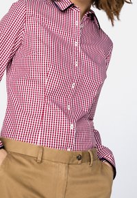 Punavalkoruudullinen kauluksellinen nappipaita, jossa on tummansininen yksityiskohta kaulassa. Yhdistetty beigen värisiin housuihin, jotka ovat vartalonmyötäiset.