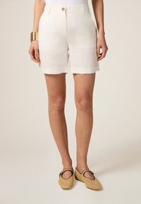 Linnen shorts in licht crème, met een opgerolde zoom, zijzakken en een knoopsluiting. Gecombineerd met geweven instappers.