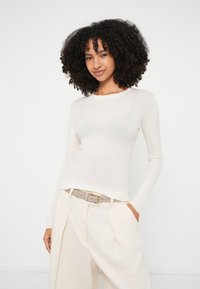 Top de manga comprida leve em creme com textura canelada, combinado com calças largas bege claro e um cinto simples com fivela circular.
