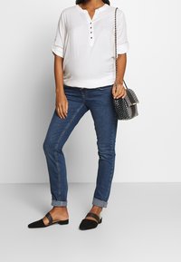 Camisa blanca de cuello con botones, jeans ajustados azules, mules negros con una correa y un bolso negro y blanco con un patrón y cadena.