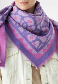 Een lila en roze gestructureerde sjaal met franjes, met bloemmotieven en geometrische ontwerpen, gedrapeerd om de nek over een lichte top.