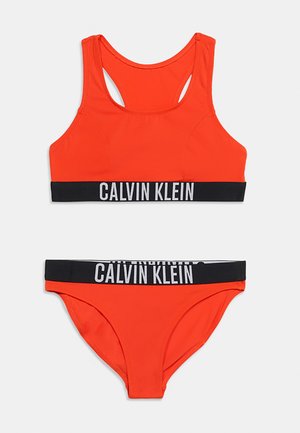 Lyse oransje to-delt bikini sett med svarte elastiske bånd med hvit "Calvin Klein" tekstlogo på toppen og bunnen.