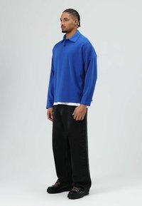 Blauw poloshirt met lange mouwen en kraag, gecombineerd met losse zwarte broek en zwarte plateau schoenen met roze veters. Eenvoudig ontwerp, casual pasvorm.
