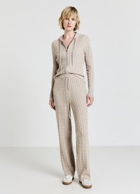 Set di abbigliamento da casa lavorato a maglia color beige, composto da felpa con cappuccio e zip con motivo a trecce e pantaloni con coulisse. Texture morbida, vestibilità ampia e maniche lunghe.