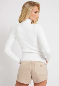 Maglione bianco a collo alto con texture a costine, silhouette aderente e maniche lunghe, abbinato a pantaloni corti beige con orlo sfrangiato.