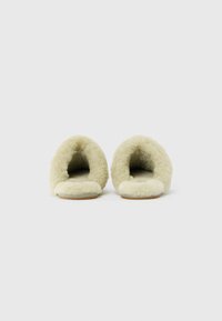 Een paar beige pluizige slippers met open hielen, weergegeven van de voorkant op een plain witte achtergrond.