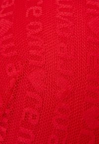 Rood gestructureerde stof met een gaasachtig patroon met subtiele letters. Het materiaal lijkt zacht en lichtgewicht, ideaal voor kleding.