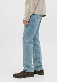 Blugi de denim albastru deschis au un design cu picior drept, cinci buzunare și cusături subtile. Purtați cu pantofi din piele maro închis.