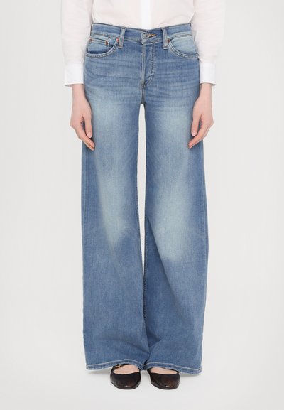 Lichtblauwe wijde jeans van denim, met een vijf-pocketontwerp en subtiele vervaging. Gecombineerd met zwarte platte schoenen.