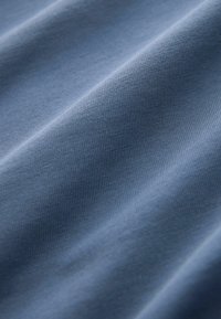 Gros plan d’un tissu bleu lisse et doux avec une texture fine en maille et de légers plis à la surface.