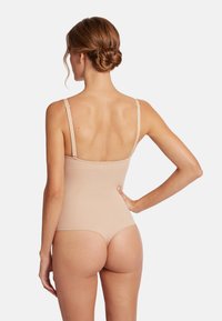 Naakt bodysuit met dunne bandjes, een gladde textuur en een aansluitend ontwerp dat het lichaam vormt. De achteraanzicht benadrukt de lage uitsnijding en naadloze afwerking.