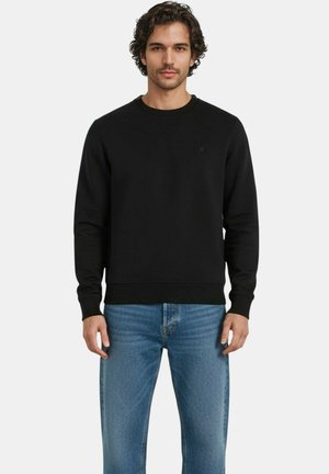 Sweatshirt noir avec un col rond et des poignets côtelés, associé à un jean en denim bleu clair, offrant une coupe décontractée et un minimum de détails.