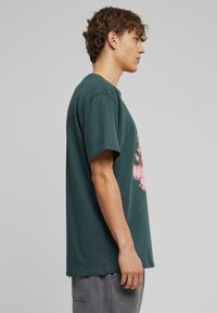 Grøn bomulds T-shirt med rund hals og korte ærmer. Med pink grafisk design på forsiden. Enkel, afslappet pasform.