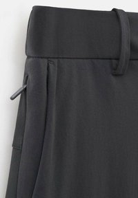 Gros plan sur un pantalon noir avec une ceinture pliée, une fermeture éclair latérale et une passants de ceinture sur le côté droit.