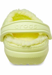 Crocs gialli con un interno morbido e peloso e una fascia posteriore, dotati di suole testurizzate e un esterno liscio. Logo visibile sulla fascia.