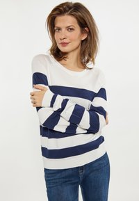 Langärmeliger Pullover mit breiten, navyblauen und weißen horizontalen Streifen, rundem Halsausschnitt und weichem Strickgewebe. Kombiniert mit blauen Jeans.