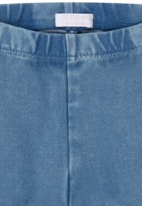 Lichtblauwe denimstof met een gestructureerde afwerking, voorzien van een elastische tailleband en een gestikte naad in het midden. Merkenlabel zichtbaar.