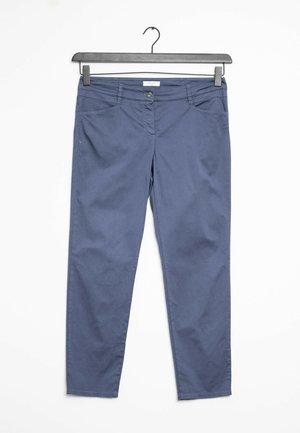 Pantalon bleu slim avec poches avant et fermeture par bouton suspendu sur un cintre noir sur fond blanc.