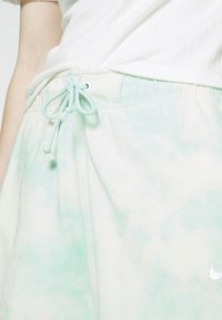 Světlé zelené šortky v technice tie-dye s elastickým pasem a šňůrkou, s malým bílým logem vlevo dole. Měkký bavlněný materiál.