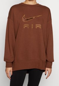 Sudadera oversized marrón con puños y dobladillo de canalé, que presenta un logo dorado de Nike y el texto "AIR" bordado en dorado a juego.
