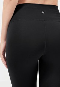 Zwarte leggings van elastisch materiaal, met een hoge taille, een gladde textuur en een minimalistisch design met een klein logo op de achterkant.