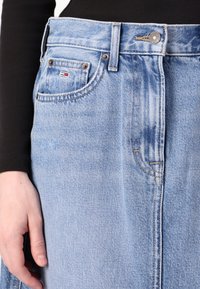 Lyseblå denim-skjørt med høy midje, frontknapplukking og sidelommer. Stoffet har en subtil falmet tekstur og sydd detaljer.