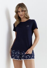 Granatowa bawełniana koszulka z krótkim rękawem, okrągłym dekoltem i małym białym logo. Połączona z granatowymi szortami w kwiatowy wzór z koronkowym wykończeniem.