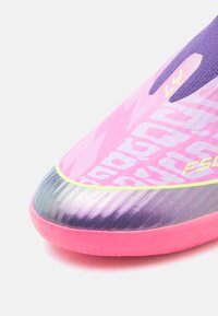 Primo piano della punta di una scarpa da calcio rosa e viola con suola testurizzata e marchio stampato sul materiale superiore.