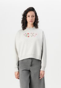 Lichtgrijze sweatshirt met bloemenborduursel op de borst, geribbelde halslijn en manchetten, en een cropped zoom. Gecombineerd met grijze wijde broek.