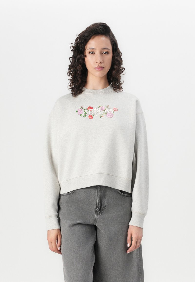 Lichtgrijze sweatshirt met bloemenborduursel op de borst, geribbelde halslijn en manchetten, en een cropped zoom. Gecombineerd met grijze wijde broek.