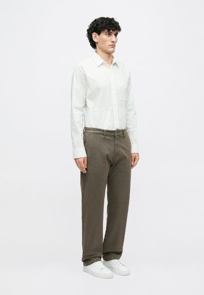 Λευκό μακρυμάνικο πουκάμισο, ελαφρύ ύφασμα, σχέδιο με κουμπιά. Ελιόχρωμο παντελόνι, casual εφαρμογή, συνδυασμένο με λευκά αθλητικά παπούτσια. Απλή, μοντέρνα εμφάνιση.