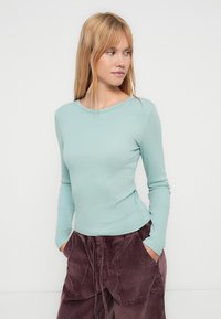 Φωτεινό γαλάζιο μακρυμάνικο μπλουζάκι με ριμπ ύφανση, στρογγυλή λαιμόκοψη, εφαρμοστή γραμμή και απαλό υλικό, συνδυασμένο με μπορντό παντελόνι από κοτλέ με τσέπες.