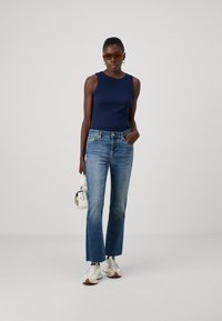 Marinblus utan ärmar, ljusblå utsvängda jeans, vita sneakers och en liten vit handväska. Tillbehören inkluderar bruna solglasögon.