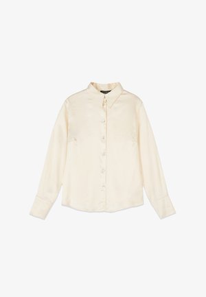 Chemise à manches longues de couleur crème, boutonnée, avec col pointu et boutons nacrés, étalée à plat sur un fond blanc.