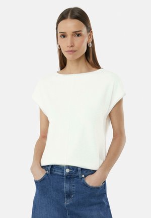Haut court à manches courtes blanc texturé avec un col bateau, associé à une jupe en denim bleue. Présente une coupe décontractée et des poches sur la jupe.
