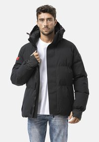 Schwarze isolierte Jacke mit hohem Kragen, Reißverschluss und Daumenlöchern an den Bündchen. Mit elastischen Akzenten und einer Seitentasche ausgestattet.